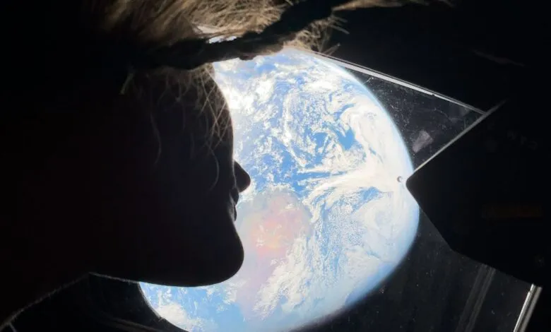 Silhouette of person gazing at Earth from spacecraft window.