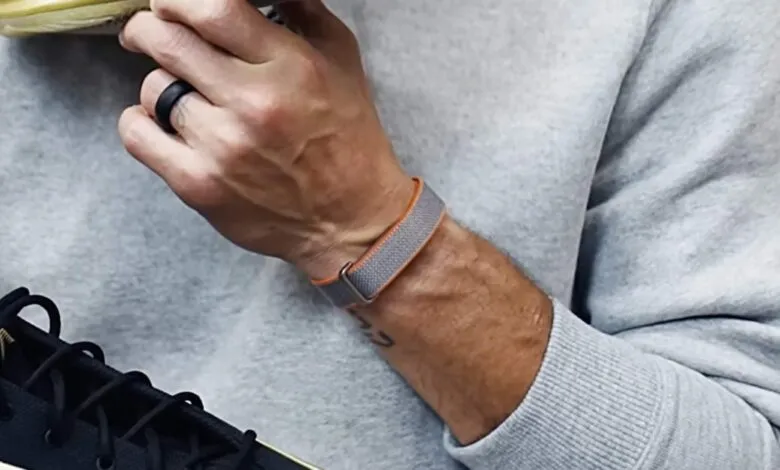 Close-up of a person wearing a gray and orange Fitbit band, holding a shoe.