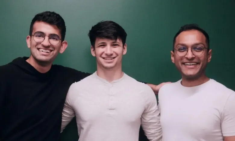 Three smiling men stand with arms around each other against a green wall.