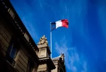 French flag waving atop a building against a bright blue sky.