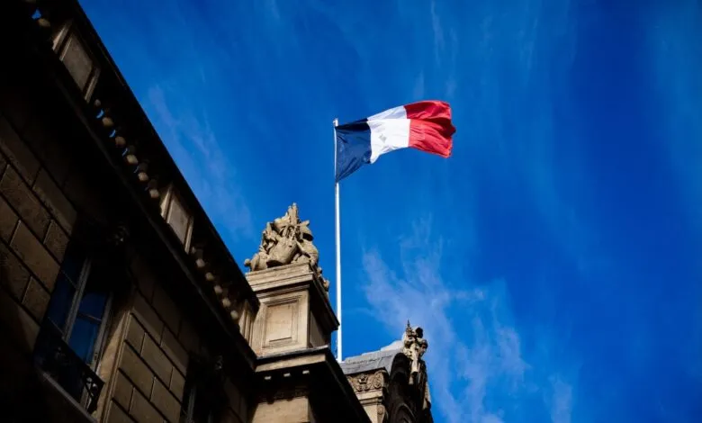 French flag waving atop a building against a bright blue sky.