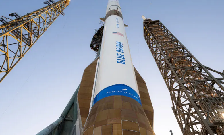 Blue Origin rocket on launchpad, surrounded by support towers, against a clear sky.