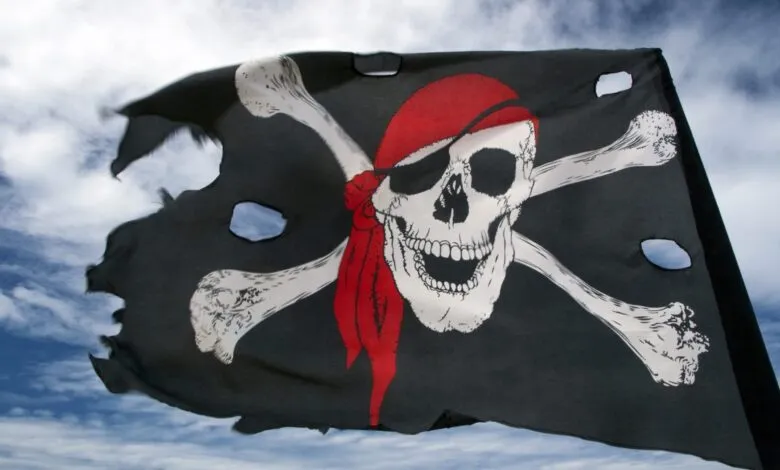 Torn pirate flag with skull and crossbones waving against a cloudy sky.