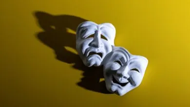 Comedy and tragedy masks on yellow background, casting a shadow.