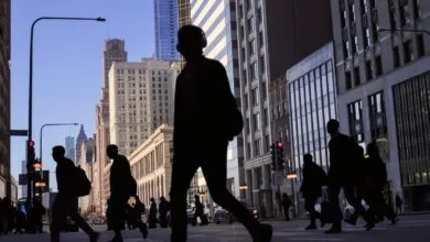 Silhouetted pedestrians cross a busy Chicago street with tall buildings in the background.
