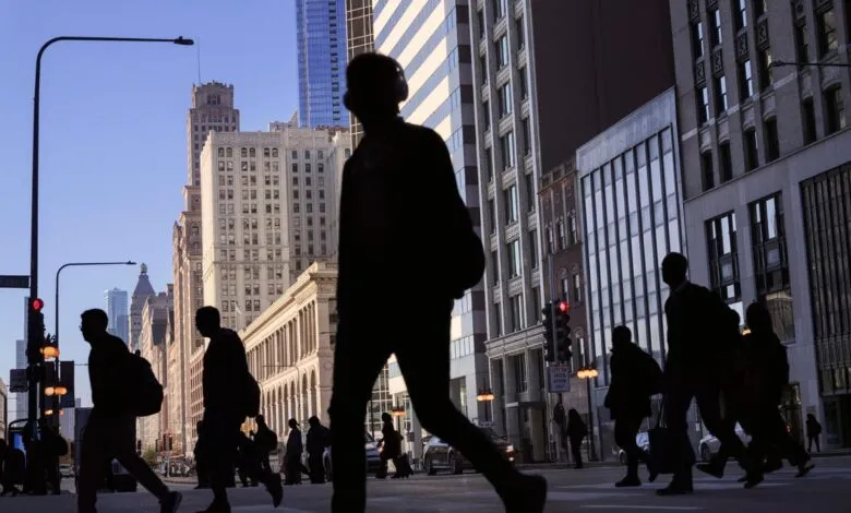 Silhouetted pedestrians cross a busy Chicago street with tall buildings in the background.