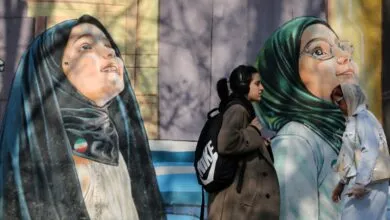 Two women walk past murals of women in hijabs on a sunny day.