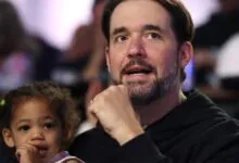 Man with beard and young child look on intently in a crowd.