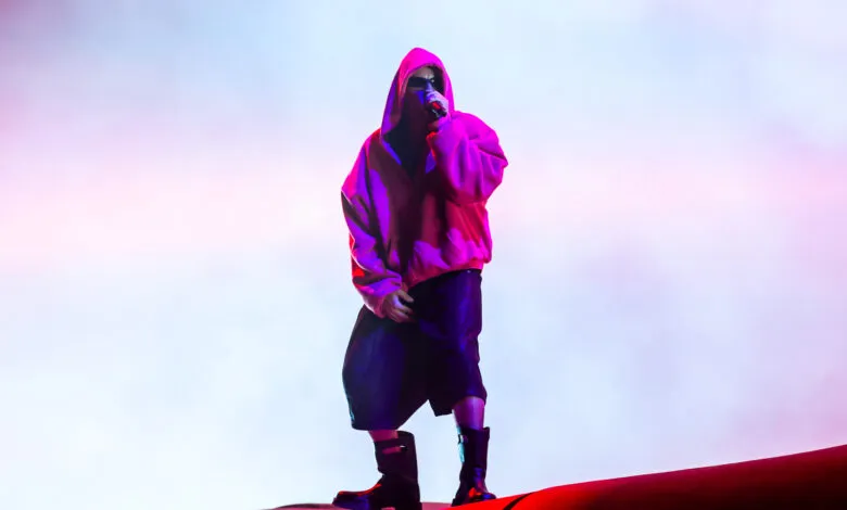 Justin Bieber performs on stage in a pink hoodie and sunglasses.