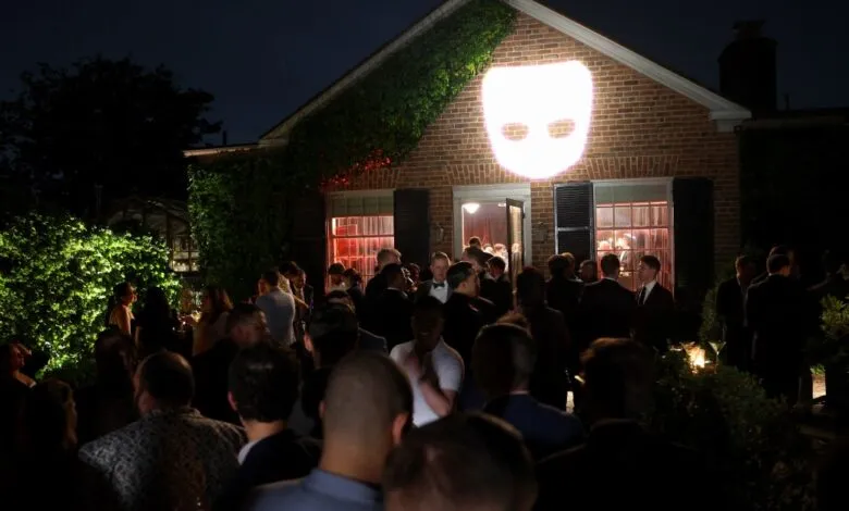 Outdoor party at night with crowd and projected face on brick building.