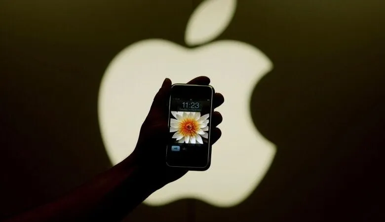 Hand holds iPhone with flower wallpaper in front of Apple logo.