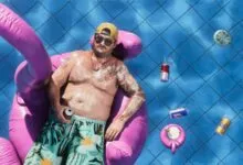 Man relaxes in pool on flamingo float with drinks and blue tiles.