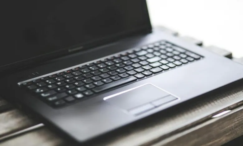 Close-up of a black laptop keyboard and trackpad on a wooden surface.