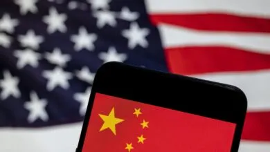 Smartphone displays Chinese flag with US flag blurred in background.