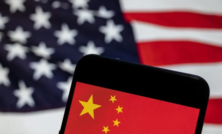 Smartphone displays Chinese flag with US flag blurred in background.