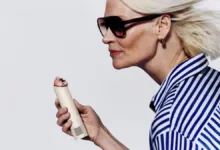 Woman with sunglasses holds a personal care device, looking to the left.