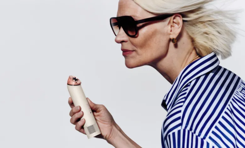 Woman with sunglasses holds a personal care device, looking to the left.