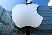 Apple logo on a glass building reflecting city architecture.