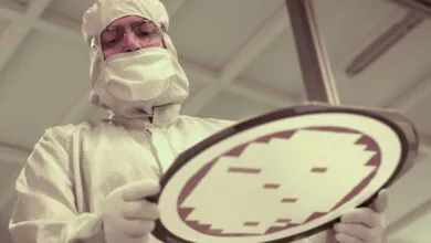 Technician in cleanroom suit inspecting a silicon wafer.