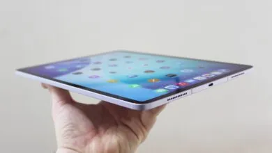 Hand holding a thin, light purple iPad Air showing the home screen.