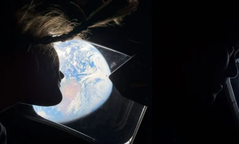 Two silhouettes look out at Earth from a spacecraft window.