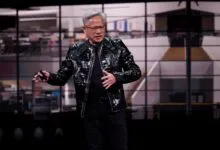Jensen Huang presents in black jacket on stage with blurred background.