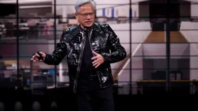 Jensen Huang presents in black jacket on stage with blurred background.