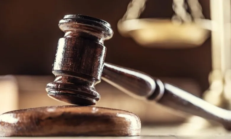 Wooden gavel rests on block with scales of justice in background.