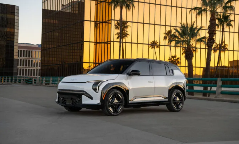 White Kia EV3 parked against golden building with palm trees.