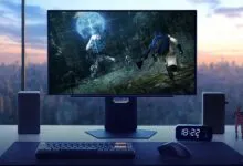 Gaming setup with monitor displaying Elden Ring, keyboard, mouse, speakers, and city view.