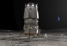 Lunar lander on the moon with two astronauts and Earth visible in the sky.