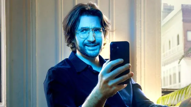 Man with glasses takes selfie indoors with a smartphone.