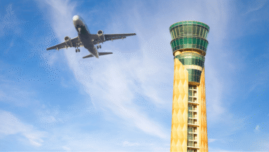 Airplane approaching airport control tower against a blue sky.