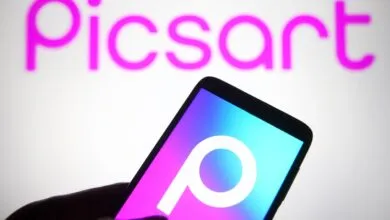 Hand holding phone displaying Picsart logo against blurred Picsart background.