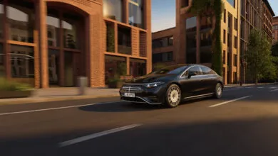 Black Mercedes-Benz EQS driving on city street with brick buildings.
