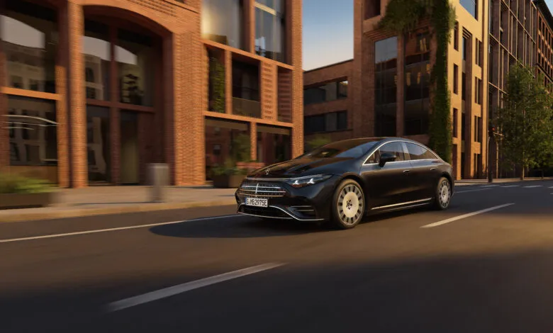 Black Mercedes-Benz EQS driving on city street with brick buildings.