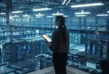Woman with tablet overlooking a large server room through glass.