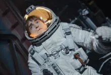 Robert Pattinson in spacesuit looks up with concerned expression.