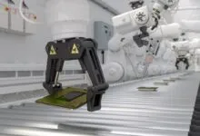 Robotic arm holding a computer chip on a conveyor belt.
