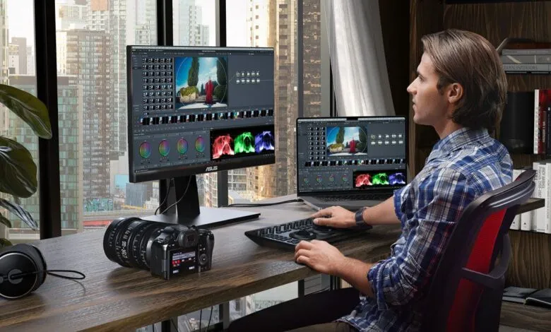 Man color grading video on dual monitors with camera and headphones on desk.