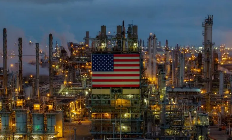 Industrial plant with US flag at night, illuminated with lights.