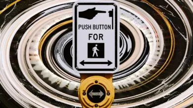 Crosswalk button with hand pushing button, pedestrian symbol, and arrows.