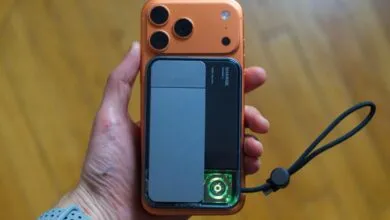 Hand holding orange iPhone with gray and black SHARGE charging accessory.