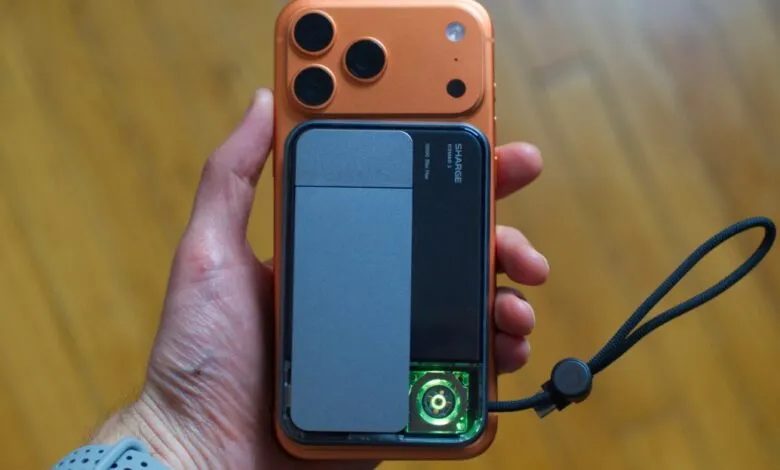 Hand holding orange iPhone with gray and black SHARGE charging accessory.