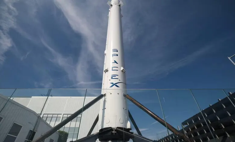 SpaceX rocket stands tall against a blue sky with wispy clouds.