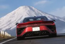 Rear view of a red sports car driving towards a snow-capped mountain.
