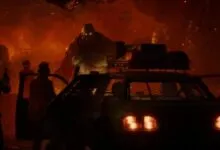 Survivors face a massive zombie near a vehicle in a fiery, post-apocalyptic scene.