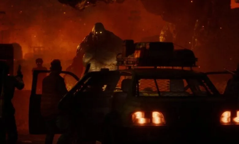 Survivors face a massive zombie near a vehicle in a fiery, post-apocalyptic scene.