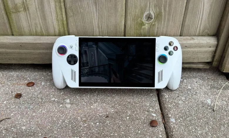 White handheld gaming PC displaying a game, resting against a wooden fence.