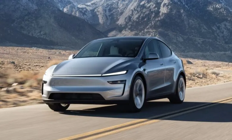 Silver Tesla Model Y driving on a road with mountains in the background.